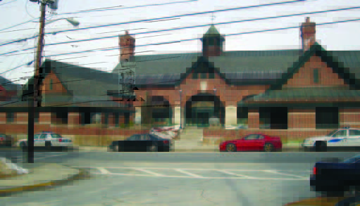 armand (1) A brick building with a central entrance, cars parked in front, and power lines crossing overhead.