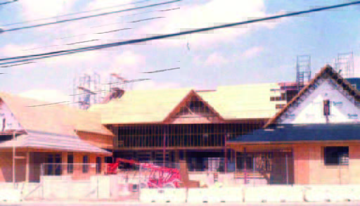 armand (2) A building under construction with exposed wooden framing and scaffolding, seen from across the street on a sunny day.