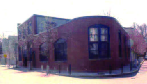 carriage (2) A brick building with large windows on a street corner, surrounded by leafless trees and a few bollards.