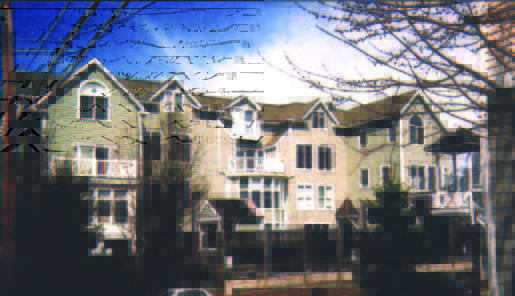 richdale (2) Three-story beige townhouse complex with peaked roofs and balconies, seen on a sunny day with bare tree branches in front.