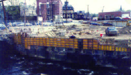 riverwalk (1) Construction site with formwork along a riverbank, buildings and parked cars visible in the background.