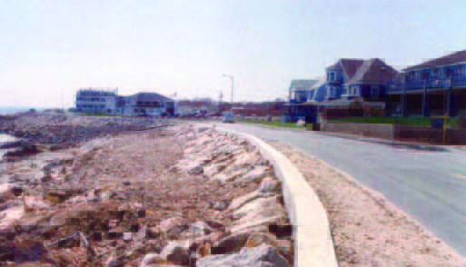 seawall (1) A paved road runs alongside a rocky shoreline with houses and buildings on the opposite side.